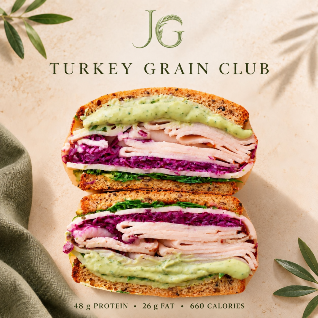 Two halves of a Turkey Grain Club sandwich layered with sliced turkey, purple cabbage, leafy greens, cheese, and creamy green dressing on multigrain bread. Contains 48 g protein, 26 g fat, and approximately 660 calories.